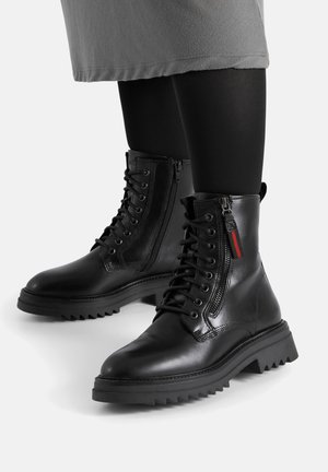 Czarne skórzane botki za kostkę z fakturowaną powierzchnią, z przodu sznurowane i z bocznym zamkiem. Posiadają masywną podeszwę z ząbkowanym brzegiem.