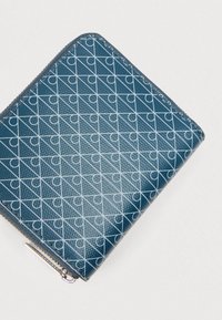 Μπλε πορτοφόλι με φερμουάρ από υλικό με υφή, που διαθέτει γεωμετρικό μοτίβο από λευκές γραμμές και κύκλους, με μεταλλικά εξαρτήματα ασημί τόνο και ραμμένες άκρες.