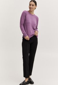 Lila gestrickter Pullover mit gerippten Bündchen, kombiniert mit schwarzen Slim-Fit-Hosen und schwarzen Slippern, die ein nahtloses Design und seitliche Schlitze aufweisen.