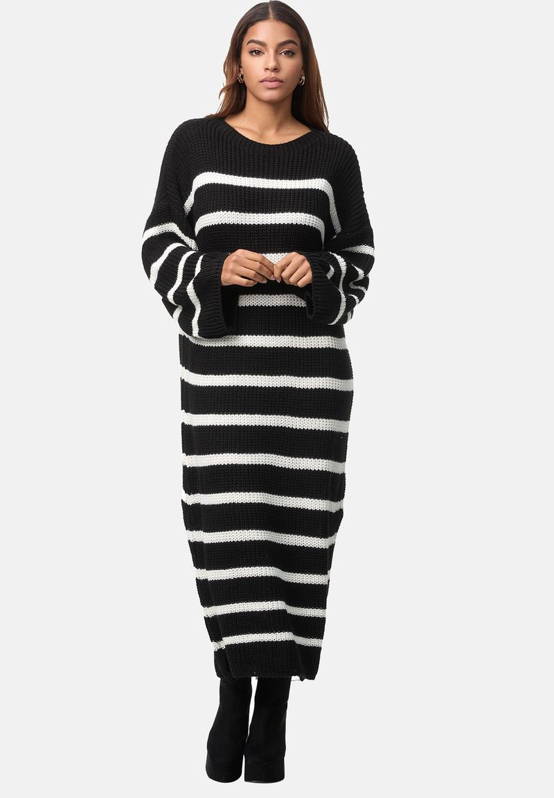 Gestreiftes, schwarzes und weißes Strickkleid mit langen, weiten Ärmeln und Rundhalsausschnitt, das bis zur Hälfte der Wade reicht, kombiniert mit kniehohen schwarzen Stiefeln.