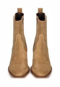 Botines de ante color tostado con punta afilada, cortes laterales y detalles de costura. Presentan una textura suave y un tacón bajo apilado.