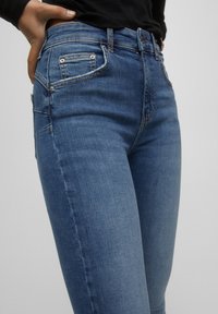 Blauwe denim jeans met een slim fit, voorzien van voorzakken, achterzakken met metalen klinknagels en een ritssluiting. Glad textuur en klassiek ontwerp.