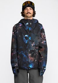 Veste noire avec un motif floral bleu et violet, dotée d'une fermeture éclair, d'une capuche et de poignets élastiques. Tissu texturé et coupe décontractée.
