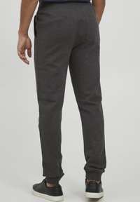 Dark gray sweatpants made of soft fabric, featuring tapered legs, elastic waistband, and side pockets. Black sneakers visible at the bottom.