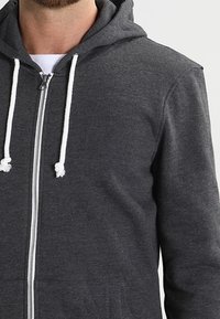 Felpa grigia con zip realizzata in un mix di cotone, con zipper frontale, lacci bianchi e tasca a marsupio.