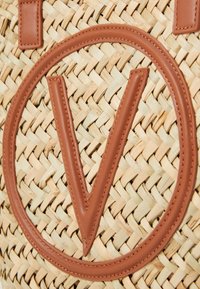 Geflochtene Strohtasche mit dem auffälligen braunen Leder-"V"-Logo, sicheren Ledergriffen und einem texturalen Kontrast zwischen den Fasern.