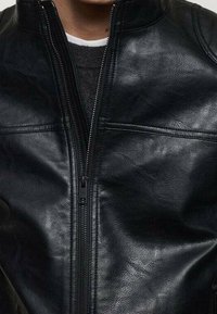 Giacca di pelle nera con colletto alto, chiusura frontale con zip, due tasche orizzontali e dettagli a superficie texturizzata.