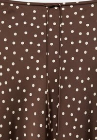 Brown fabric with evenly spaced white polka dots and a centered thin drawstring tied loosely at the top.
