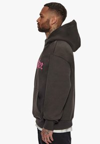 Hoodie de magasin en mélange de coton gris foncé, doté d'un logo brodé rose, d'une poche avant et d'une capuche à cordon réglable.