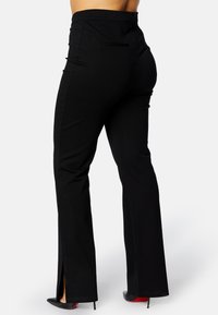 Zwarte taillerende broek met een aansluitende taille, voorzien van zijsplitsen aan de zoom en slanke stof, met een gladde textuur en een gestructureerd ontwerp.