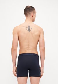 Marinefarbene Boxershorts mit einem strukturierten Bund, körpernaher Passform und Logo-Details, die oben sichtbar sind. Die Haut ist auf dem nackten Rücken des Models zu sehen.