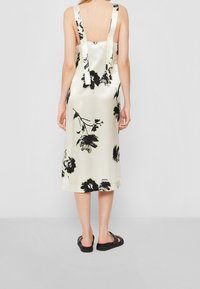 Saténové midi šaty s květinovým černým potiskem. Mají široké ramínka, odhalená záda a rovný střih. Barva je světle krémová s elastickým detailem.