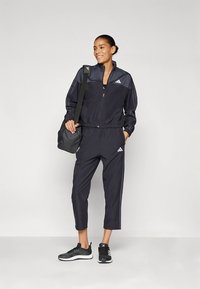 Czarny sportowy dres z kurtką na zamek i skróconymi spodniami, z elastycznym pasem i akcentami logo Adidas. Do kompletu czarne sneakersy.