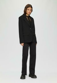 Schwarzer übergroßer Blazer mit aufgesetzten Taschen, einem Knopf und Reverskragen, kombiniert mit schwarzen Jeans und klobigen schwarzen Schuhen.
