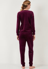 Purple velour pajama set featuring a long-sleeve top with round neckline and matching pants. Smooth texture, casual design, fitted silhouette.
