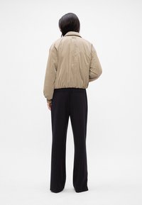 Beige bomber jacket with a relaxed fit, gathered hem, and ribbed cuffs, paired with black pinstripe trousers, seen from the back.