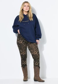 Felpa oversize blu navy con testo dorato, abbinata a leggings leopardati marrone e nero e stivali da cowboy marroni. Tessuto morbido, vestibilità comoda.