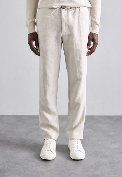 Linnedragter i lys beige med snøre i taljen, slim fit, parret med hvide sneakers, har et enkelt design og glat tekstur.