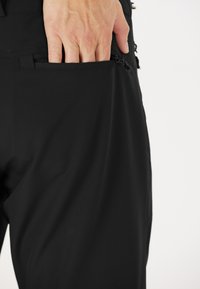 Svarta byxor i mjukt, elastiskt tyg, med en sidoficka med dragkedjestängning och subtila sömnadsdetaljer längs sömmarna.