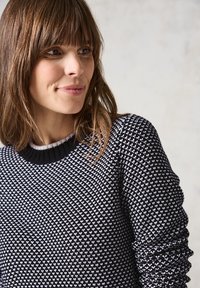Pull en noir et blanc avec un motif, doté d'un design en tricot texturé et d'un col côtelé. Vue rapprochée montrant le détail du tissu et de l'ajustement.