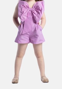 Fioletowy kombinezon z dużą kokardą przy dekolcie, z dwiema bocznymi kieszeniami i gładką, błyszczącą fakturą. Noszony z złotymi płaskimi butami.
