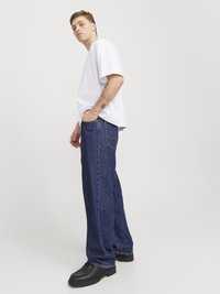 T-shirt blanc à manches courtes et jeans larges bleu marine. Chaussures noires à finition lisse. Design droit, coupe décontractée, détails minimaux.
