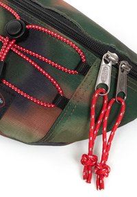 Custodia con motivo camouflage, dotata di una cerniera nera, dettagli in corda rossa e tiranti metallici. Presenta un tessuto testurizzato e dettagli con corda elastica regolabile.