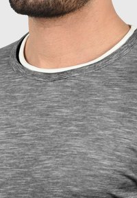 Grå heathered t-skjorte med rund hals, med en kontrasterende hvit indre krage og fin tekstur. Nærbilde av stoffet.