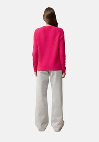 Fuchsia gebreide trui met een ronde hals, textuurstof en lange mouwen, gecombineerd met lichtgrijze wijde broek.
