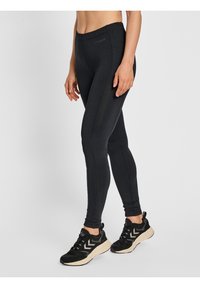 Svarta leggings med en mjuk textur, med hög midja och sidficka. Matchas med svarta träningsskor.