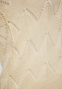 Strikket beige tekstil med et zigzag-mønster og åbne masker, der har en blød tekstur og let design velegnet til lagdeling.