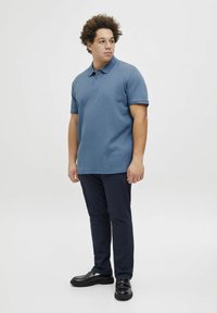 Blauwe polo met een gestructureerde stof, korte mouwen en een kraag. In combinatie met donkerblauwe broeken en zwarte schoenen.