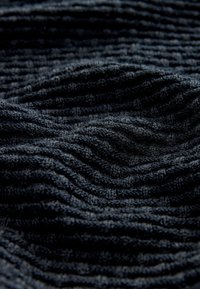 Teksturirana temno modra tkanina z valovitim vzorcem. Material deluje mehak, z izbočenimi črtami, ki ustvarjajo globino in vizualni interes.