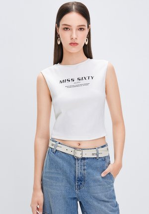 Hvid ærmeløs crop top med "MISS SIXTY" trykt i sort, parret med højtaljede blå denim jeans og et lysfarvet bælte.