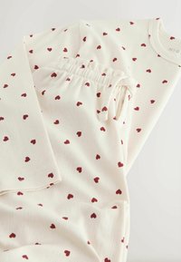 Valge kangast ööpükside komplekt punaste südamemustritega, millel on pika varrukaga topp ja elastse vöökohtaga püksid, millel on peened triibud.