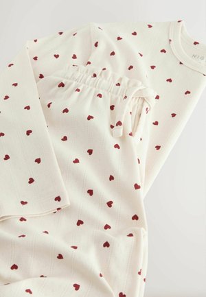 Valkoinen kangaspuku yöpaitana, jossa on punaisia sydänkuvioita, sisältäen pitkähihainen paita ja elastisella vyötäröllä varustetut housut, joissa on hienovaraisia viivoja.