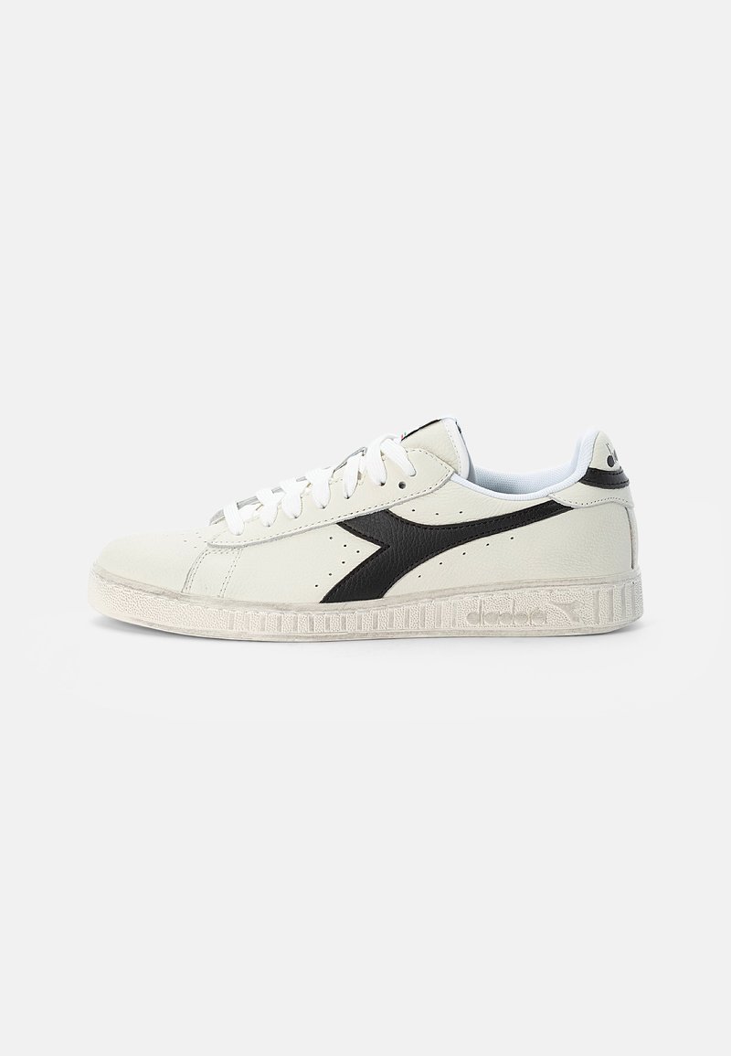 White leather sneaker with black accents, rounded toe, and flat laces. Features a textured sole and small perforations for ventilation.