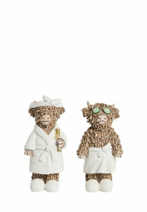 Two textured brown cow figurines in white spa robes and slippers; one holds a glass and wears a towel headband, the other wears green eye patches.