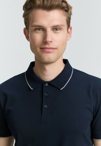 Navy poloshirt van katoen met een klassieke kraag, vijf knopen en een contrasterende grijze bies op de kraag. Glad textuur, aansluitend ontwerp.