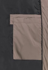 Zwarte buitenstof met een beige opbergzak met een rechthoekige klep en gestikte randen. Sooie textuur met minimale hardware.