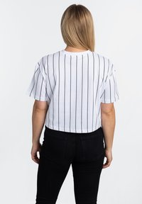 Weißes, kurzes T-Shirt mit vertikalen schwarzen Streifen, kurzen Ärmeln und rundem Halsausschnitt. Getragen mit schwarzen Hosen.