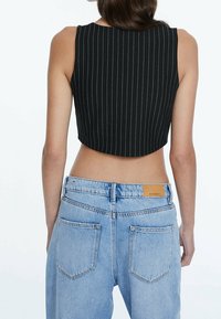 Schwarzes, kurzes Tanktop mit weißen vertikalen Streifen, Rückansicht, kombiniert mit hellblauen, hoch taillierten Jeans aus Denim mit Lederpatch.