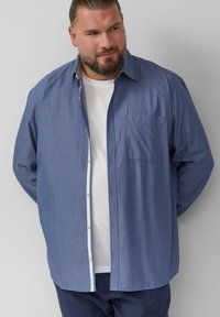 Camicia azzurra con bottoni, decorata con piccoli pois bianchi, colletto appuntito, taschino sul petto e dettagli a contrasto all'interno del colletto.