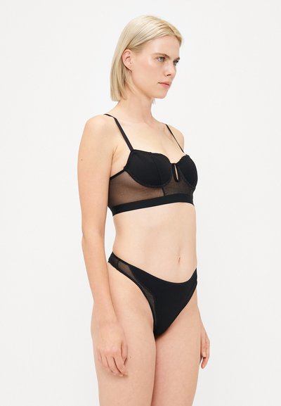 Zwarte lingerie set met een gepadde bralette met doorschijnende zijpanelen en bijpassende hoge slips, die een minimalistisch ontwerp benadrukt.