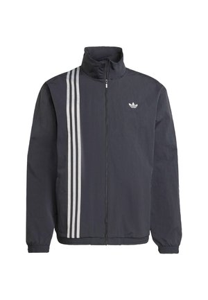 Veste noire zippée avec col montant, présentant trois bandes verticales blanches sur le côté gauche et un petit logo sur la poitrine. Matériau léger.
