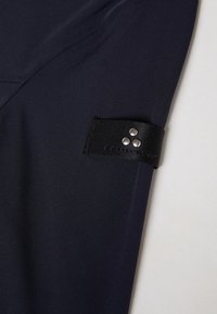 Navy fabric with a smooth texture, featuring a black strap on the sleeve accented by three silver studs for fastening.