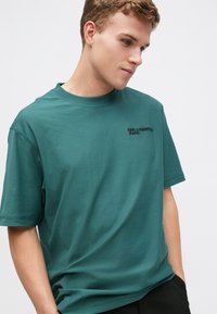 Smaragdovo zelené bavlnené tričko s okrúhlym výstrihom, krátkymi rukávmi a jemným čiernym logom "KARL LAGERFELD JEANS" na hrudi. Hladká textúra.