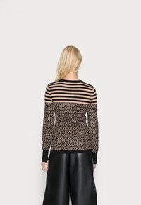 Maglione a righe nero e marrone con motivo ripetuto del logo “GUESS”, caratterizzato da maniche lunghe e collo a coste, abbinato a pantaloni neri a gamba larga.