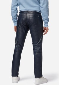 Navy leren broek met een gladde textuur, slim fit, twee achterzakken en stiksels. Gecombineerd met een lichtblauwe trui en witte sneakers.