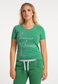 Grön bomullst-shirt med rund halsringning och korta ärmar. Framsidan visar silverfärgad text i olika storlekar.